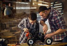 Image of a father and son work on a remote controlled scale model car in a workshop, as part of a blog about creating a scale modelling workspace.